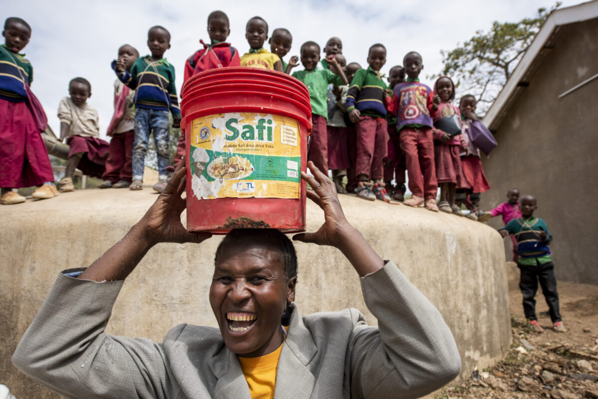 A woman holds a bucket over her head by a rainwater harvesting tank at a primary school in Tanzania.