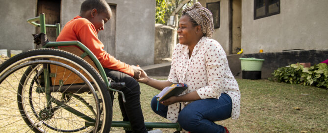 Cleo, a nurse, talks to Debora in her wheelchair outside a home in Tanzania.