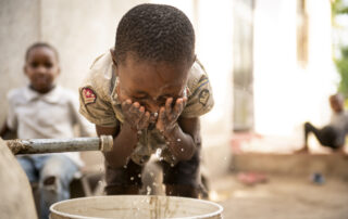 A child splashes his face with water from a rainwater harvesting system outside his home in Tanzania.