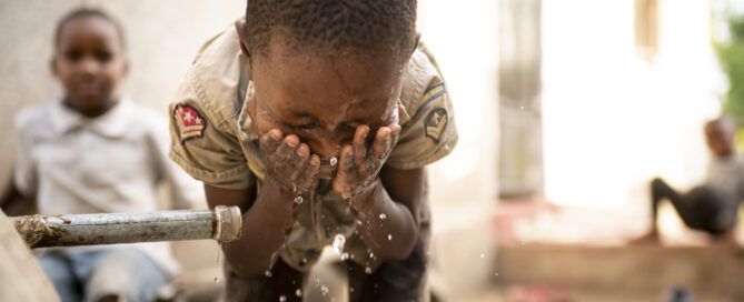 A child splashes his face with water from a rainwater harvesting system outside his home in Tanzania.