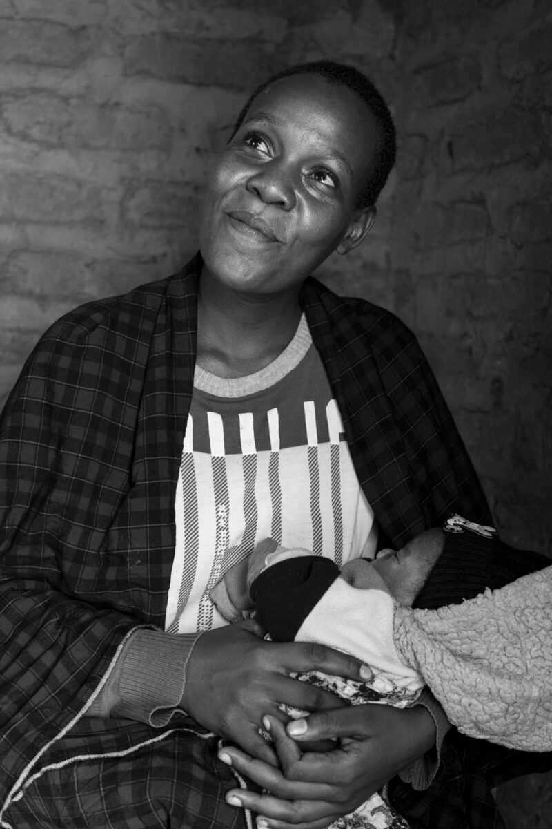 A woman smiles softly while cradling a sleeping baby wrapped in a blanket.