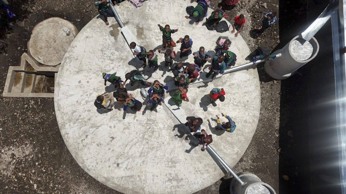 Aerial view of a group of children standing on a large circular concrete platform, looking up at the camera.