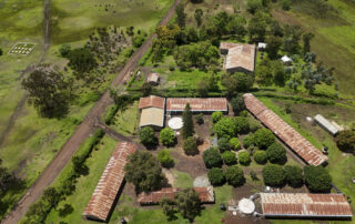 Aerial view of a rural farm with red-roofed buildings, dirt roads, and green fields.