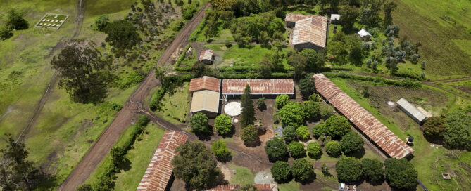 Aerial view of a rural farm with red-roofed buildings, dirt roads, and green fields.