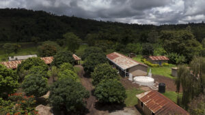 Rural village with red-roofed houses amid dense trees and green hills under a cloudy sky
